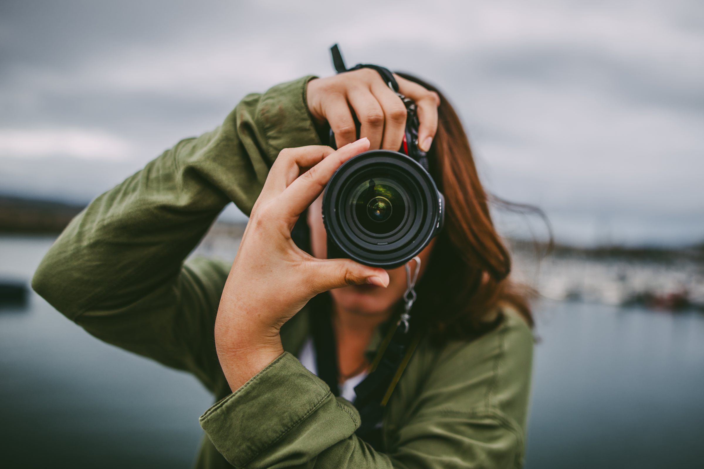 Frau fotografiert mit einer Spiegelreflexkamera direkt in die Linse – Sinnbild für den Fokus auf Projekte